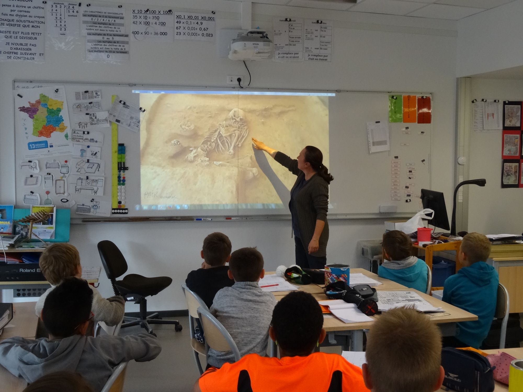 Groupe d'élèves en classe devant un tableau, le professeur commente une image de squelette